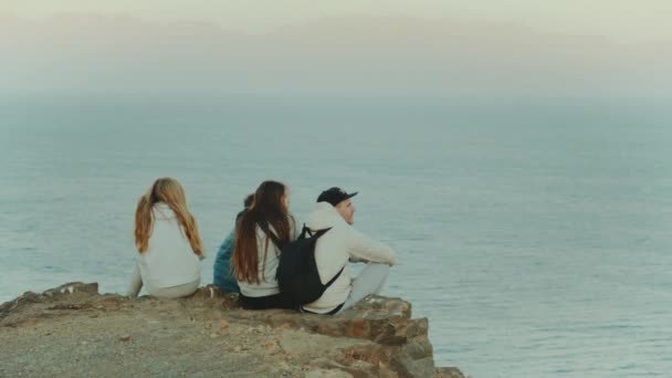 Ομάδα φίλων που χαλαρώνουν στην κορυφή ενός βουνού στο ηλιοβασίλεμα και απολαμβάνουν θέα στη θάλασσα - φιλία, νεολαία, 4k — Αρχείο Βίντεο