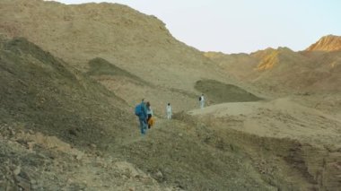 Bir grup turist sıcak çölde kaya kanyonu boyunca yürür, turistler fotoğraf çeker ve eğlenirler. Çöl Dağları, Mısır, Sina, 4k