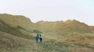 Bir grup turist sıcak çölde kaya kanyonu boyunca yürür, turistler fotoğraf çeker ve eğlenirler. Çöl Dağları, Mısır, Sina, 4k