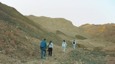 Bir grup turist sıcak çölde kaya kanyonu boyunca yürür, turistler fotoğraf çeker ve eğlenirler. Çöl Dağları, Mısır, Sina, 4k