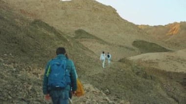 Bir grup turist sıcak çölde kaya kanyonu boyunca yürür, turistler fotoğraf çeker ve eğlenirler. Çöl Dağları, Mısır, Sina, 4k