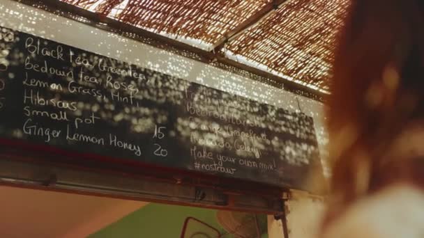 Vista posterior de la mujer cliente mirar el menú en la pared en la tienda vegetariana elegir bebida, zumos frescos en el menú en la tienda Dahab, Egipto, 4k — Vídeos de Stock