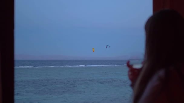 Mulher beber vinho e veja como as pessoas Kite surf em água limpa bonita em Dahab Egito. Explorando o mar azul com montanhas no fundo e pessoas kite surf, 4k — Vídeo de Stock
