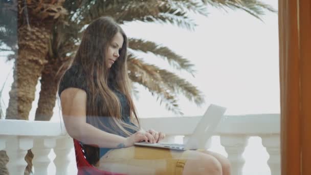 Schöne Studentin oder Freiberuflerin, die an einem Laptop arbeitet, Frau, die auf einem Balkon mit Blick auf Palme und Meer sitzt, voll hd — Stockvideo