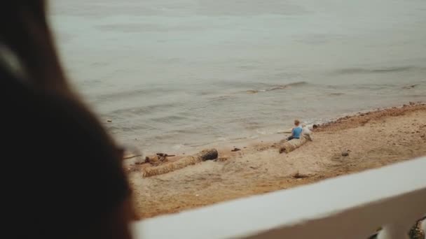 Samotna kobieta przebywająca na balkonie i do błękitnego morza, dzieci bawią się na plaży w pobliżu morza, pełne hd — Wideo stockowe