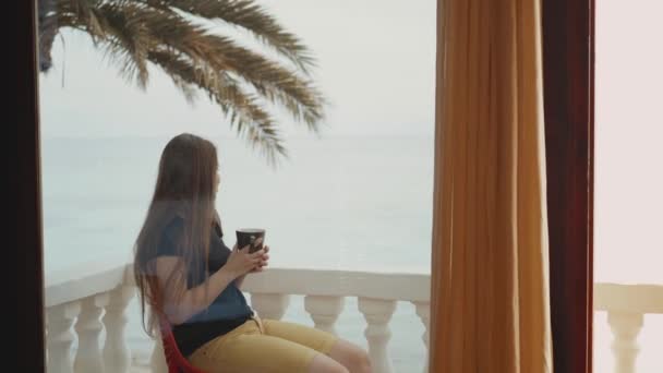 Donna sola sta bevendo caffè o tè al mattino sul balcone con vista mare blu, punto di vista dalla finestra, hd completo — Video Stock