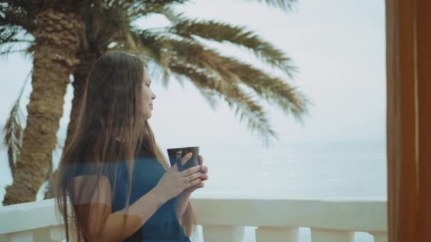 Samotna kobieta pije rano kawę lub herbatę na balkonie z niebieskim widokiem na morze, punkt widzenia z okna, pełny hd — Wideo stockowe