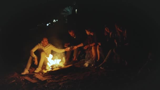 Bir grup arkadaş, gece boyunca deniz kenarında kamp ateşinin yanında eğleniyorlar. — Stok video