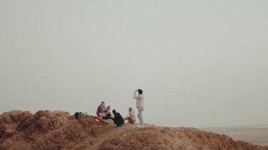 Gün batımında bir dağın tepesinde dinlenen bir grup insan, şenlik ateşinin yanında oturmuş, zamanlarının tadını çıkarıyorlar - arkadaşlık, gençlik, tam kapasite.
