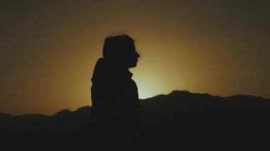 Gün batımında çölde yürüyen güzel genç bir kadının silueti. Çölde gezen bir kadın, kum tepeleri, rüzgar esintisi, tam yol ileri.