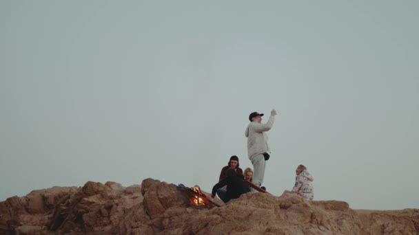Gruppo di persone che si rilassano sulla cima di una montagna al tramonto, seduti vicino al falò, godendo il loro tempo amicizia, gioventù, hd completo — Video Stock