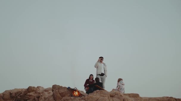 Grupo de personas que se relajan en la cima de una montaña al atardecer, sentados cerca de la hoguera, disfrutando de su tiempo - amistad, juventud, full hd — Vídeos de Stock