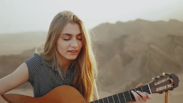 Mulher tocando guitarra e cantando no deserto em paisagens do pôr do sol, deserto montanhas fundo, hd completo — Vídeo de Stock