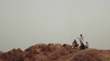 Gün batımında bir dağın tepesinde dinlenen bir grup insan, şenlik ateşinin yanında oturmuş, zamanlarının tadını çıkarıyorlar - arkadaşlık, gençlik, tam kapasite.