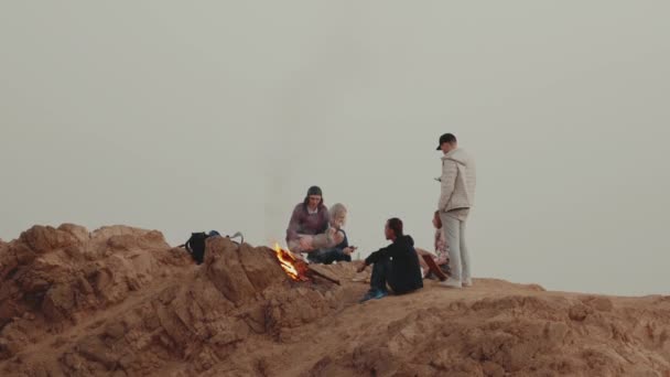 Emberek csoportja pihennek egy hegy tetején naplementekor, közel ülnek a tábortűzhöz, élvezik az idejüket - barátság, ifjúság, teljes HD — Stock videók