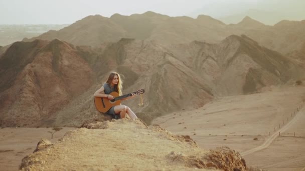 Γυναίκα παίζει κιθάρα και τραγουδούν στην έρημο σε τοπία ηλιοβασίλεμα, έρημο βουνά φόντο, πλήρη hd — Αρχείο Βίντεο