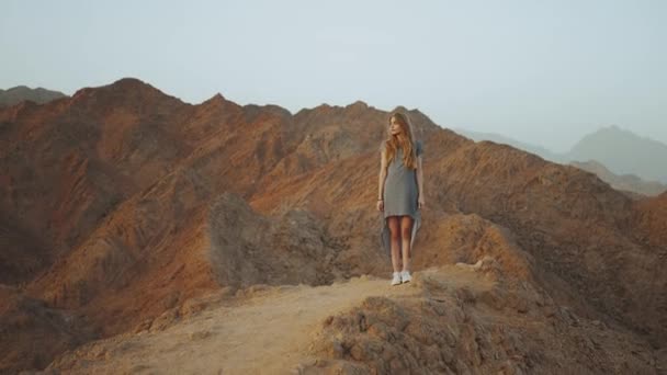 Retrato de una guapa rubia al atardecer. Feliz joven mujer de pie en una montaña del desierto, paisaje puesta de sol, hd completo — Vídeos de Stock