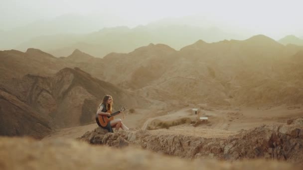 Mulher tocando guitarra e cantando no deserto em paisagens do pôr do sol, deserto montanhas fundo, hd completo — Vídeo de Stock