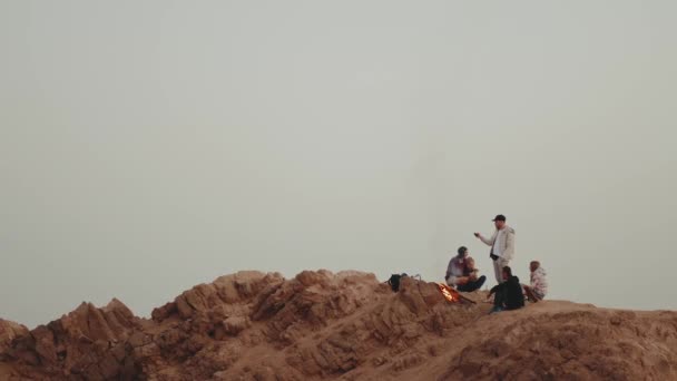 Grupo de pessoas relaxando no topo de uma montanha no pôr do sol, sentado perto de fogueira, desfrutando de seu tempo amizade, juventude, hd completo — Vídeo de Stock