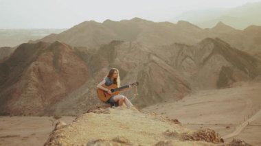 Günbatımında çölde gitar çalan ve şarkı söyleyen bir kadın.