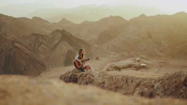 Mulher tocando guitarra e cantando no deserto em paisagens do pôr do sol, deserto montanhas fundo, hd completo — Vídeo de Stock