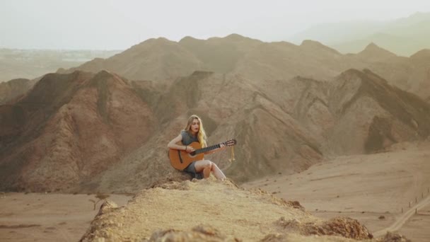 Kvinna som spelar gitarr och sjunger i öknen i solnedgången landskap, öken berg bakgrund, full hd — Stockvideo