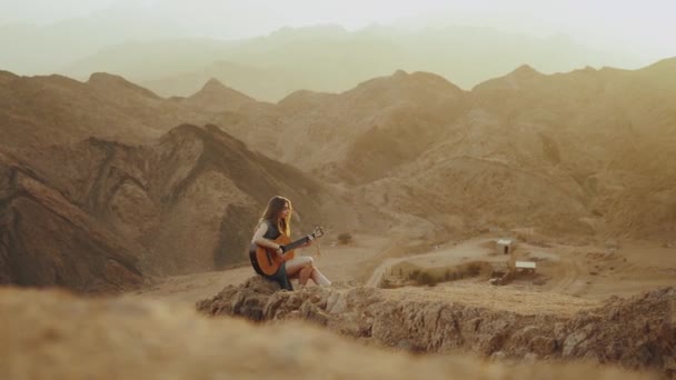 Kvinna som spelar gitarr och sjunger i öknen i solnedgången landskap, öken berg bakgrund, full hd — Stockvideo