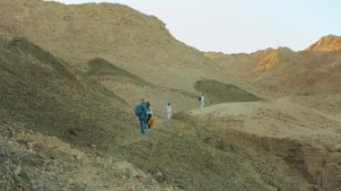 Bir grup turist sıcak çölde kaya kanyonu boyunca yürür, turistler fotoğraf çeker ve eğlenirler. Çöl Dağları arka planı, Mısır, Sina, tam HD