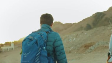 Bir grup turist sıcak çölde kaya kanyonu boyunca yürür, turistler fotoğraf çeker ve eğlenirler. Çöl Dağları arka planı, Mısır, Sina, tam HD
