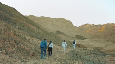 Bir grup turist sıcak çölde kaya kanyonu boyunca yürür, turistler fotoğraf çeker ve eğlenirler. Çöl Dağları arka planı, Mısır, Sina, tam HD