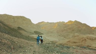 Bir grup turist sıcak çölde kaya kanyonu boyunca yürür, turistler fotoğraf çeker ve eğlenirler. Çöl Dağları arka planı, Mısır, Sina, tam HD