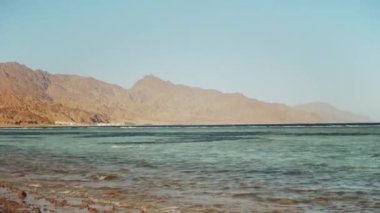 Kızıl denizde şnorkelle yüzen bir adam, güzel mavi deniz manzarası ve berrak gökyüzü, taştan bir sahile vuran dalgalar ve ufuktaki dağlar, Mısır, Dahab, tam yol.