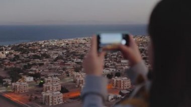 Akşamları kadın akıllı telefondan denizin fotoğrafını çeker. Kadın dağın tepesinde durur ve Horizon 'a bakar.