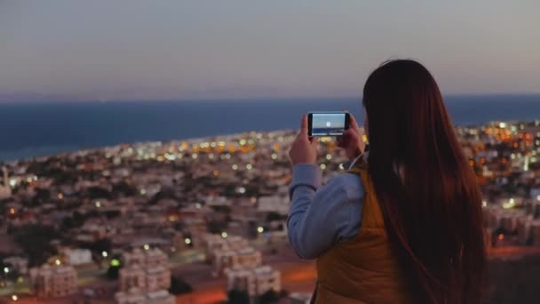 女性は夕方にスマートフォンで海の写真を撮る。女性は山の上に滞在し、地平線に見て、完全なhd — ストック動画
