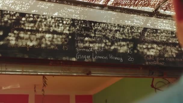 Visão traseira do homem cliente olhar para o menu na parede na loja vegetariana escolher bebida, sucos frescos no menu na loja Dahab, Egito, hd completo — Vídeo de Stock