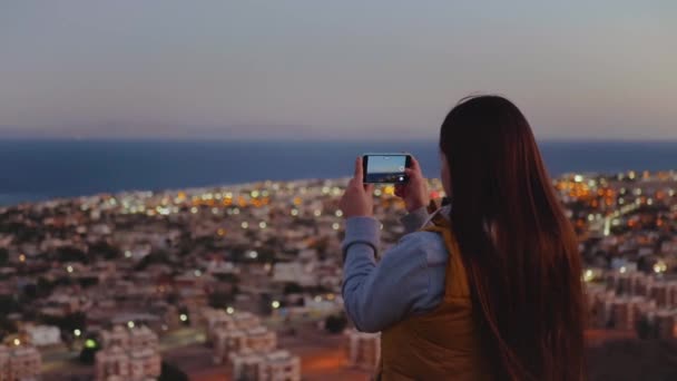 女性は夕方にスマートフォンで海の写真を撮る。女性は山の上に滞在し、地平線に見て、完全なhd — ストック動画