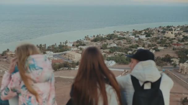 Gün batımında bir dağın tepesinde dinlenen ve deniz manzarasının tadını çıkaran bir grup turist. Dostluk, gençlik, tam kapasite. — Stok video