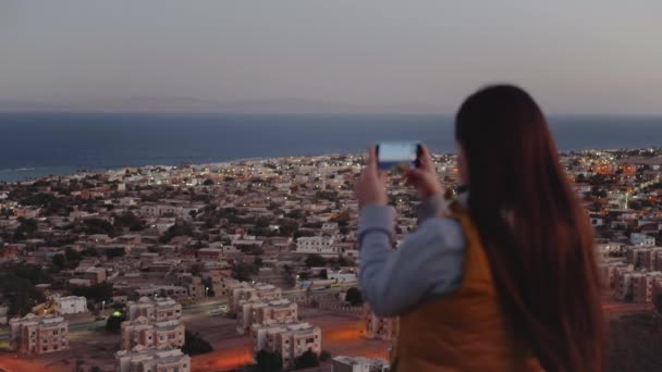 Akşamları kadın akıllı telefondan denizin fotoğrafını çeker. Kadın dağın tepesinde durur ve Horizon 'a bakar. — Stok video