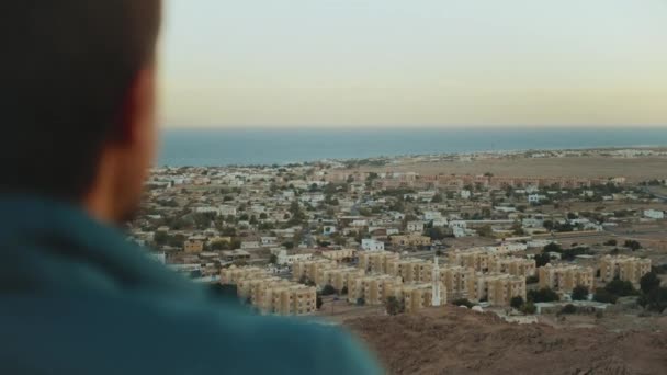 L'uomo guarda avanti verso l'orizzonte durante il tramonto, mare blu e cielo limpido, rallentatore, full hd — Video Stock