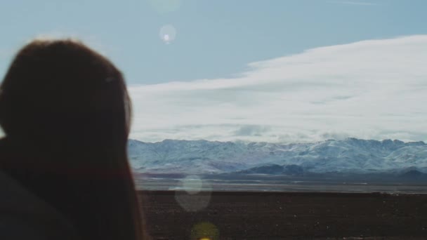 Mulher de pé e olhando para o topo das montanhas do Atlas, com picos nevados panorâmicos e céu nublado, coelhos do sol para a câmera, Marrocos, 4k — Vídeo de Stock