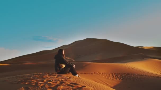 Einsam sitzt Frau auf Dünen in der Sahara Wüste bei Sonnenuntergang, Tourist sitzt allein über einem sandigen Hügel in endloser Wüste, schöne Landschaften Wüste, Marokko, 4k — Stockvideo