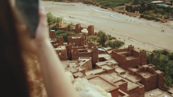 Vrouw op de foto De beroemde Ait Benhaddou Kasbah uitzicht vanaf de top, oude stad, Prachtige toeristische plaatsen van Marokko, 4k — Stockvideo