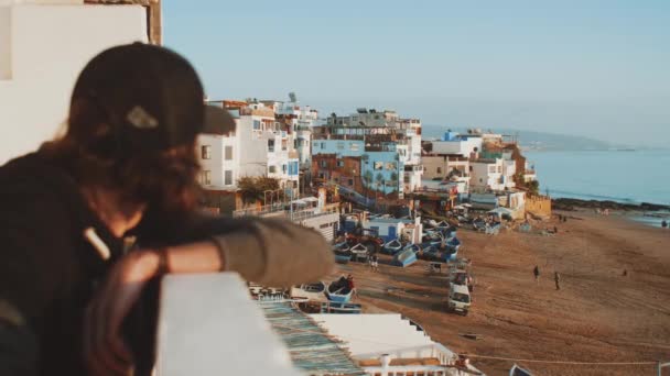 Omul de pe balcon se uită la oraş. Sat frumos și plajă mică confortabilă Oceanul Atlantic în Maroc, 4k — Videoclip de stoc