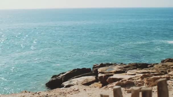 Eau de l'océan Atlantique lors d'une marée s'écrasant sur un rivage pierreux, les vagues frappent les pierres légèrement, temps ensoleillé et ciel clair, Maroc 4k — Video