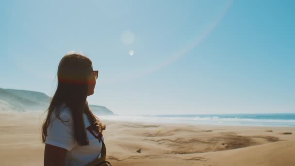 Frau mit Sonnenbrille blickt zum Horizont des Ozeans. Amazing Sand Dunes by Beautiful Blue Ocean, Dahkla, Marokko, Sonnenhasen in die Kamera, 4k — Stockvideo