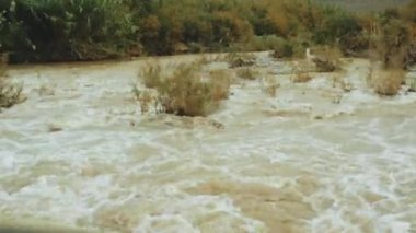 Fas 'ta çamurlu suyu olan dağ nehri, nehrin hızlı akışı, araba penceresinden manzara, hareket halinde çekim, tam yol ileri.