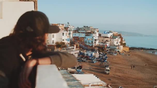 Mannen på balkongen tittar på staden. Vacker by och liten mysig strand Atlanten i Marocko, full hd — Stockvideo