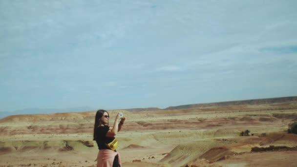 Γυναίκα με γυαλιά ηλίου που διαμένουν στους βραχώδεις λόφους και τη λήψη φωτογραφιών από το όμορφο τοπίο της ερήμου λόφους στο Μαρόκο, full hd — Αρχείο Βίντεο