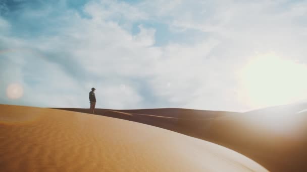 Ensam man stående i Saharaöknen vid horisonten, gyllene sand och molnig himmel. Sanddyner i arabisk öken. Sand sanddyner våg mönster. Natur bakgrund, Marocko, full hd — Stockvideo