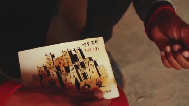 Марокканець виготовляє поштові листівки для туристів древнього фортеці Аїт Бен Хадду, бербер, Марокко поблизу Уарзазазате в Атлаських горах, повний hd — стокове відео